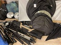 Multiple tripods and backdrop stands along with reflectors and diffuser discs laid out on floor