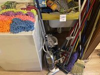 Lot of cleaning tools with vacuum, various mops and broom leaning against a wall, colorful mop heads on the top of a washing machine.