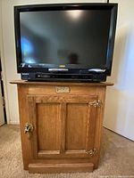 Vizio 31-inch HDTV on top of the oak storage box, Sony DVD/CD player below the TV screen visible on the box, full view of storage box showing brass hardware and plaque.