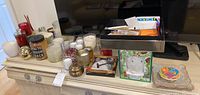 Overview showing multiple candles in various containers and a box with papers and small items on a dresser.