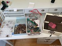 Table setup with open white jewelry box with key, large container bins holding assorted costume jewelry such as bracelets, necklaces, and earrings.