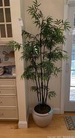 Full view of faux bamboo plant with leaves, stems and white ceramic pot, showing plant height and structure.