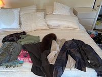 Photo showing various jackets and sweaters laid out on a bed, including different colors and materials.