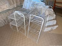 View of several white metal wire shoe racks and hanging organizers in a room with carpet and bed in background