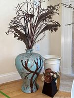 Blue ceramic vase with brown tree branch and white flower motif holding faux dried flowers.