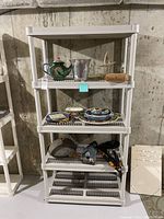 White plastic shelving unit with various household items on shelves against concrete wall.