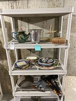 Full view of shelving with kettle, ice bucket, painted platters and bowls, bamboo basket, wooden box, wok pan, and strainer