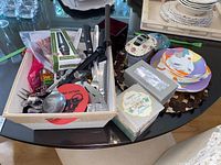 Top-down view of basket containing multiple kitchen utensils and other items on glass table with plates and coasters near
