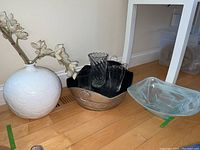 Wider view showing the white ceramic vase, oval metal container with four clear glass vases/glasses, and clear square glass bowl