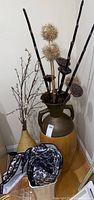 Large and small decorative vases with faux plants placed near a wall corner