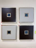All four square wall art pieces arranged on a wall: two dark brown and two light gray backgrounds with small blue inset squares in the center.