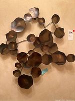 Photo of metal wall art sculpture showing clustered irregular metallic discs attached to rods, mounted on wall.