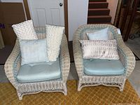 Front view of two wicker chairs with light blue cushions and various accent pillows, showcasing the overall condition and style.