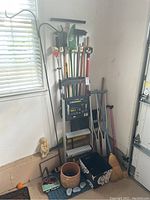 Full view photo showing yard tools, ladder, crutches, cane, clay planter, statue, mat, basket grouped in corner of room