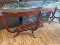 Full view of glass top wooden accent table showing its curved legs and lower shelf.