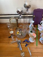 Photo showing assortment of glass candle sticks, wind chimes, glass and porcelain decorative items on wooden surface.