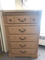 Front view showing five drawers with decorative metal drawer pulls and carved upper front edge.