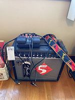 Fender Frontman 25R amplifier with Fender guitar strap and Boss foot pedal on top, cables connected but untidy, placed on wooden floor.