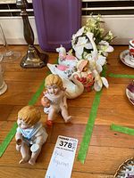 Photo of ceramic figurines on wooden surface including two seated child figurines and swan bird figurines with floral details.