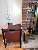 Photo showing the black metal frame wood storage bag with a brown leather sling next to the brass match holder filled with blue-tipped matches and fireplace brick hearth.