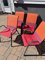 Four matching outdoor mesh chairs with metal frames and orange, pink, and purple fabric backs and seats, arranged on a stone patio.
