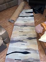 Partially unrolled runner rug showing modern abstract pattern on a wood floor near a sofa and TV.
