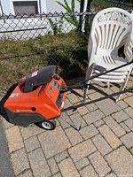 Side view of Husqvarna snow blower showing orange and black plastic body, wheels, and handle, positioned outdoors on pavers.