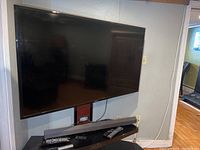 Samsung 55 inch TV wall mounted with Sony soundbar below and several remotes on the soundbar.