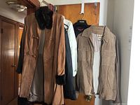 Photo showing six jackets/coats hanging on door rack including long tan suede coat with dark fur trim and toggle fasteners, and other jackets of various colors and materials