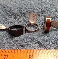 Three men's rings displayed on blue fabric, showing front and side views with size tags.