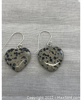 Pair of heart-shaped Dalmatian jasper stone earrings with cream base and black spots attached to sterling silver hooks, shown laying flat.