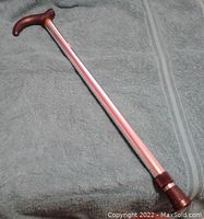 Full view of the adjustable cane laid on a towel, showing its wooden curved handle and aluminum shaft.