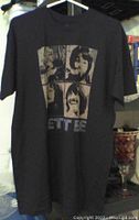 Full view front of black T-shirt on hanger showing The Beatles portraits and Let It Be text.