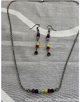Full view of necklace and earrings on fabric background showing arrangement of chakra-colored beads on silver-tone chain and earring hooks.