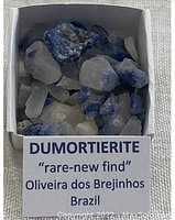 Photo showing multiple dumortierite quartz mineral specimens, highlighting the blue inclusions within white quartz matrix. Pieces vary in size and shape and are displayed in a box labelled with origin and identification.