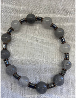 Full view of grey quartz gemstone bead bracelet with magnetic hematite and copper spacers on a white textured fabric background.