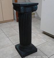 Full view of the dark and light green heavy column plant stand showing fluted shaft and square base on tile floor.