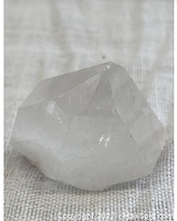 Close-up photo of the natural quartz crystal point showing the clear to milky body and natural faceted terminations on fabric background.