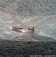 Gold tone screw stud earring shown laying horizontally on a textured gray surface, inside clear plastic packaging to maintain condition.