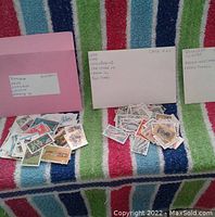 Three envelopes with assorted spent postage stamps loose in front of each. Envelope labels list countries from Africa, Caribbean, and Oceania among others.