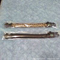 Two survival bracelets, one camouflage and one black, still in plastic packaging laid out on a blue towel.