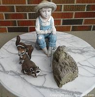 Overview of all figurines showing boy figurine, raccoon, squirrel, and frog on marble surface.