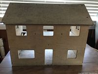 Front exterior view of a wooden two-story unfinished dollhouse showcasing multiple cut-out rectangular windows and a door.