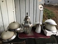 Six assorted household lighting fixtures including indoor and outdoor styles shown on an outdoor surface