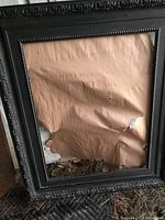 Black mirror with ornate molding and bead details. Torn and wrinkled backing paper visible through glass.
