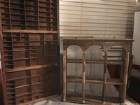 Wooden shelf with arched openings next to wooden print type case with many small compartments