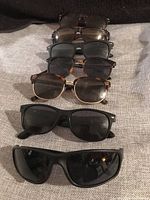 Six pairs of assorted sunglasses arranged on grey fabric, showing a variety of styles and lens colors.