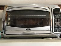 Front view of silver Oster toaster oven with digital controls on the right, glass door slightly tired and used.