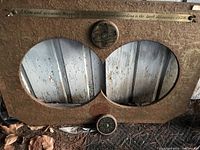 Photo showing a rectangular wooden or particle board frame with two large oval openings and compass decorative elements. Text strip at the top references a 1628 map.