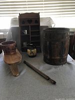 Photo showing a group of vintage country-style decorations including a wooden wall rack with heart cutouts, a large wooden bucket, a long wooden paddle, a small wooden bench, and a floral ceramic vase.